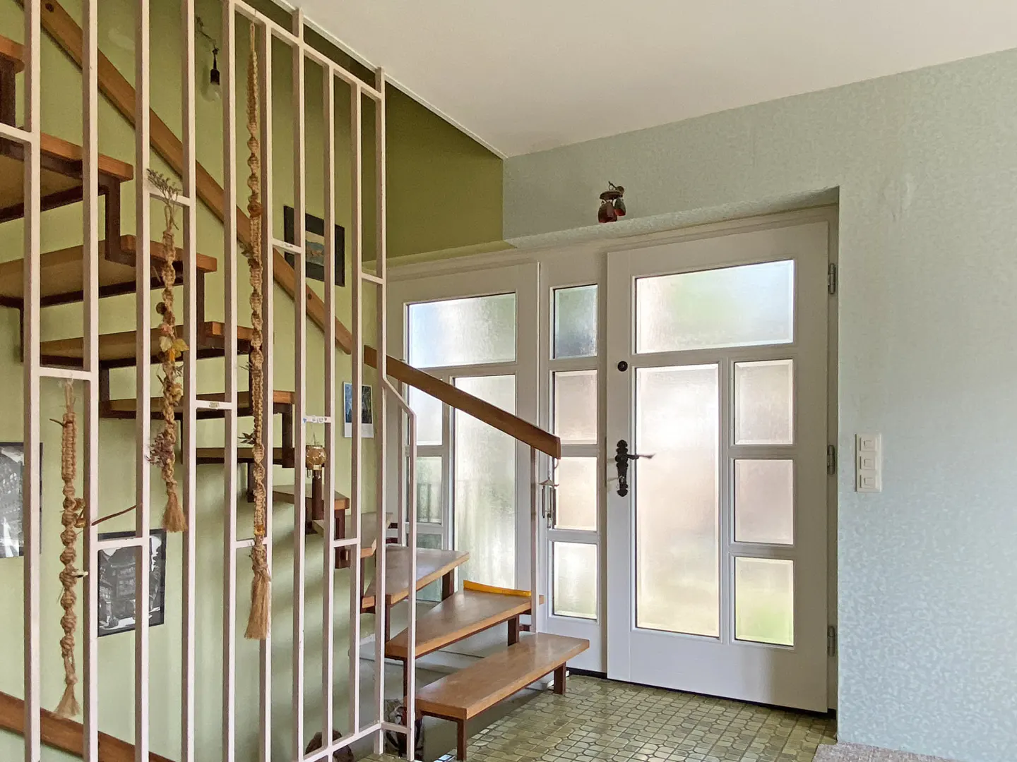 A home's entryway with a wooden staircase, white metal railing, and a white front door with frosted glass panels.