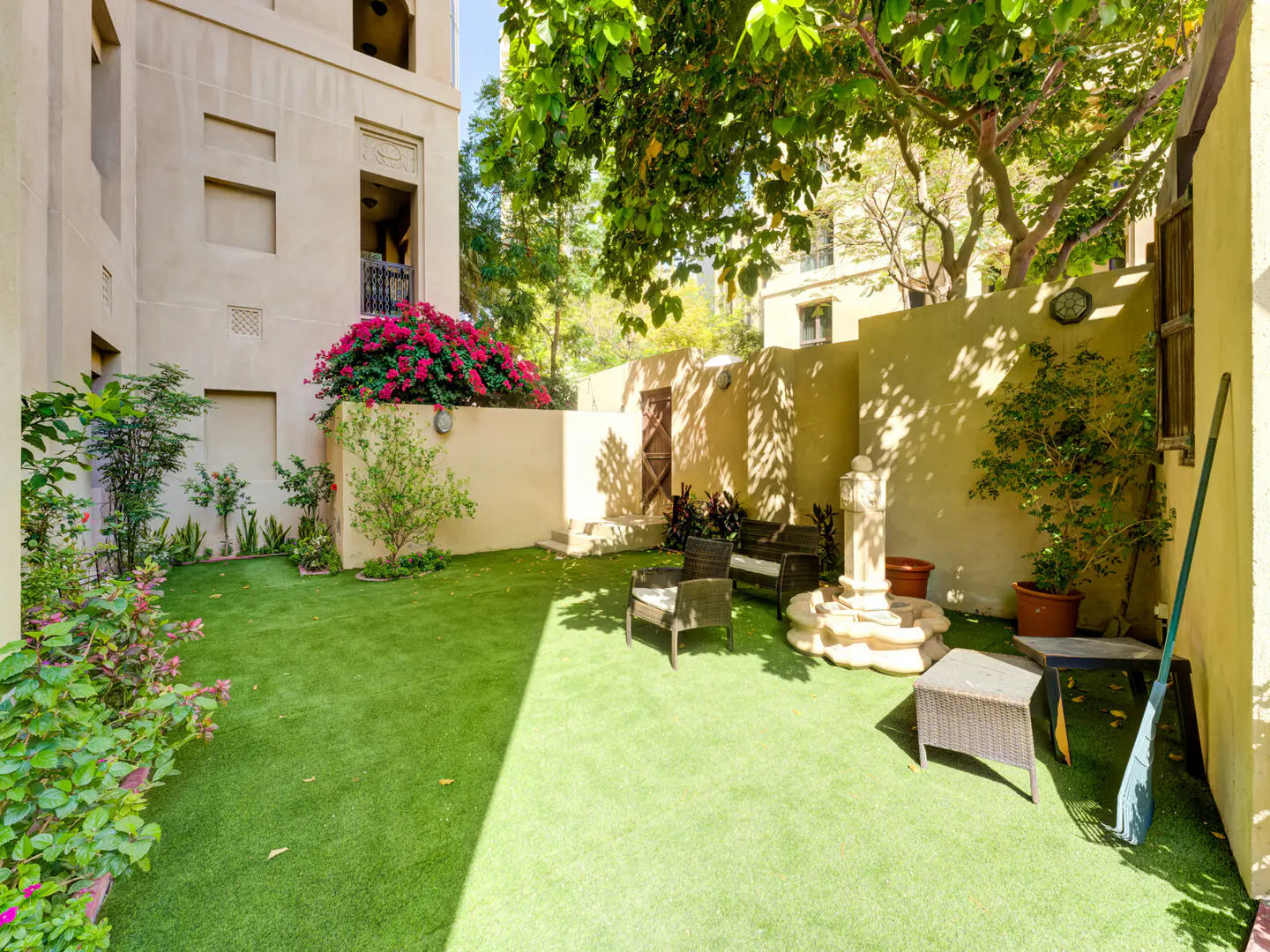 A backyard with green grass, a seating area, and a beige building in the background.