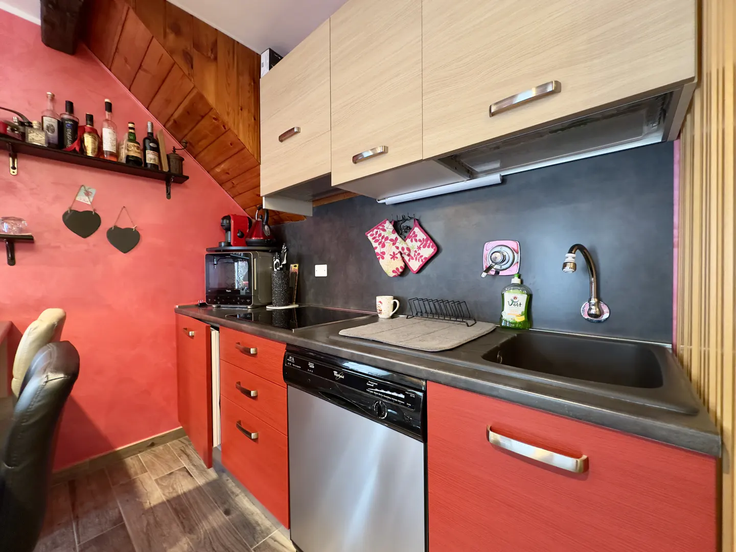 A kitchen with red cabinets, stainless steel appliances, and light wood upper cabinets.