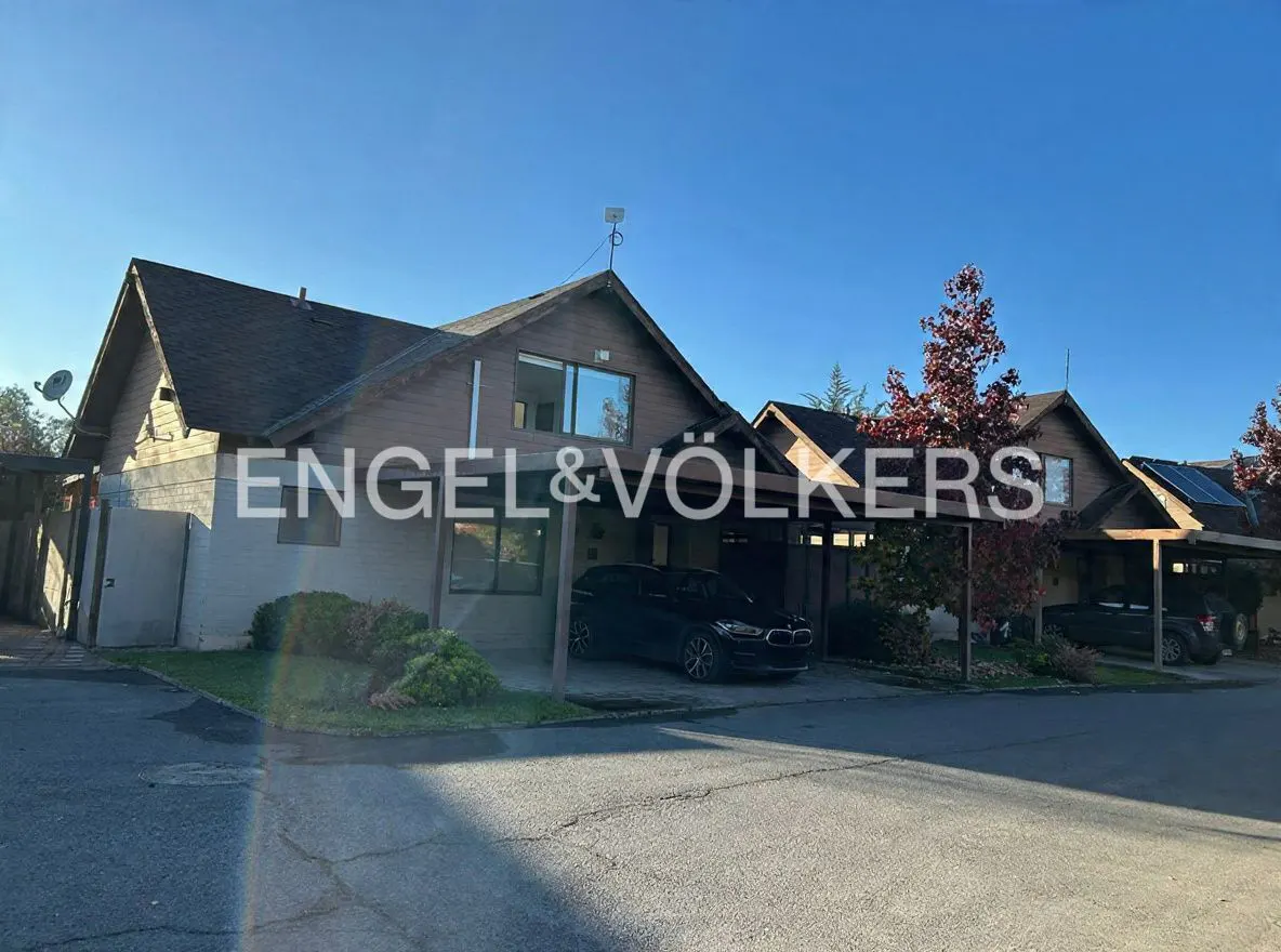 Exterior view of brown, two-story townhouses with carports and parked cars under a blue sky. Engel & Völkers logo overlay.