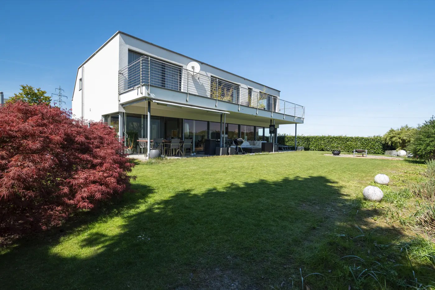 Two-story modern white house with a balcony overlooking a green lawn and a red Japanese maple tree.