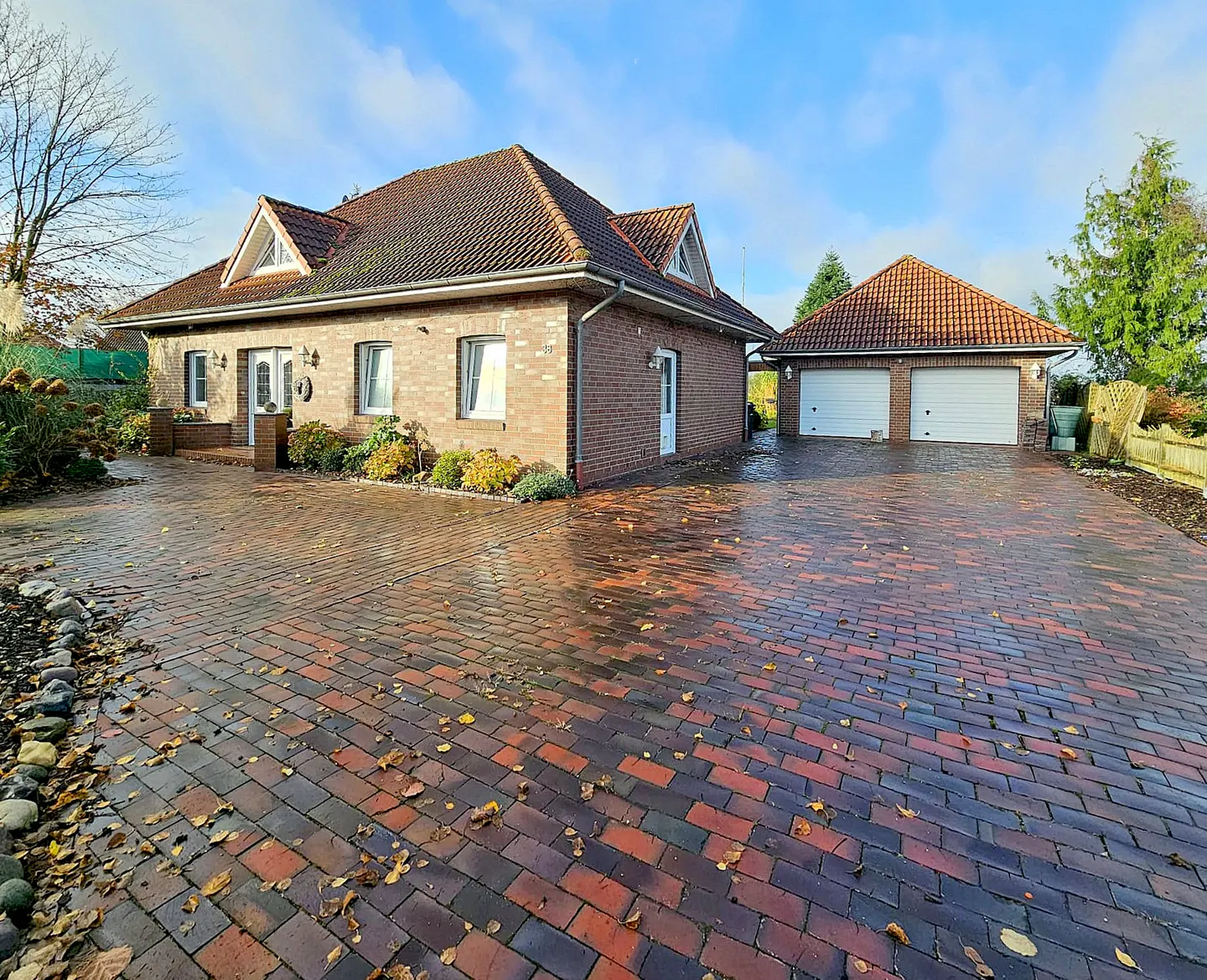 A brick house with a red tile roof and a two-car garage sits on a brick driveway.