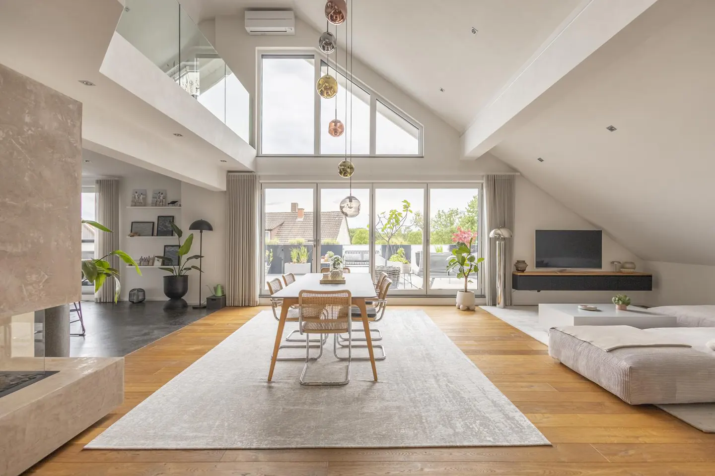Bright, open-plan living space with a dining table, sofa, and large windows leading to a balcony. Modern interior design with light wood floors and white walls.