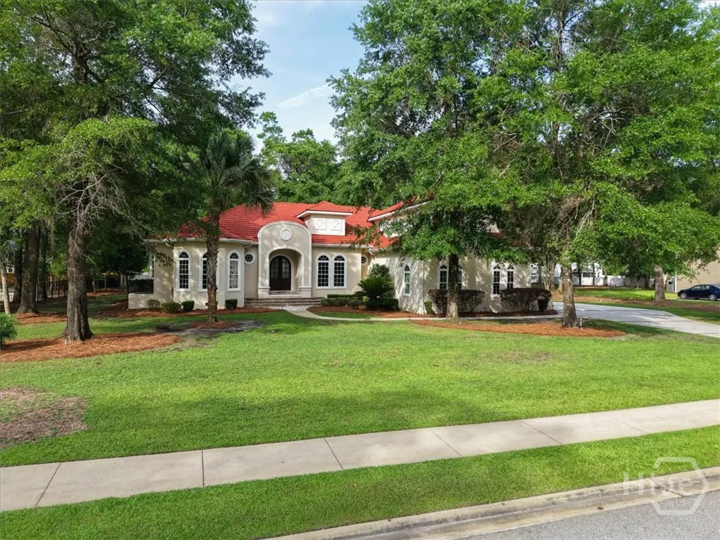 Beige house with a red roof, surrounded by green trees and a large lawn.