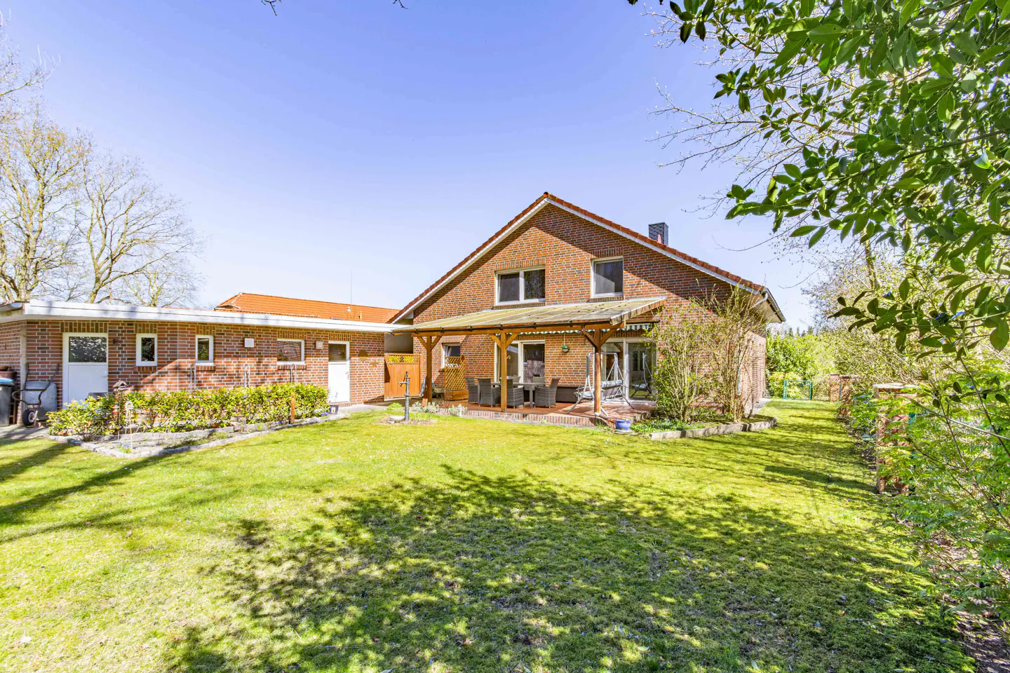 Brick house with a green lawn and a covered patio with outdoor furniture on a sunny day.