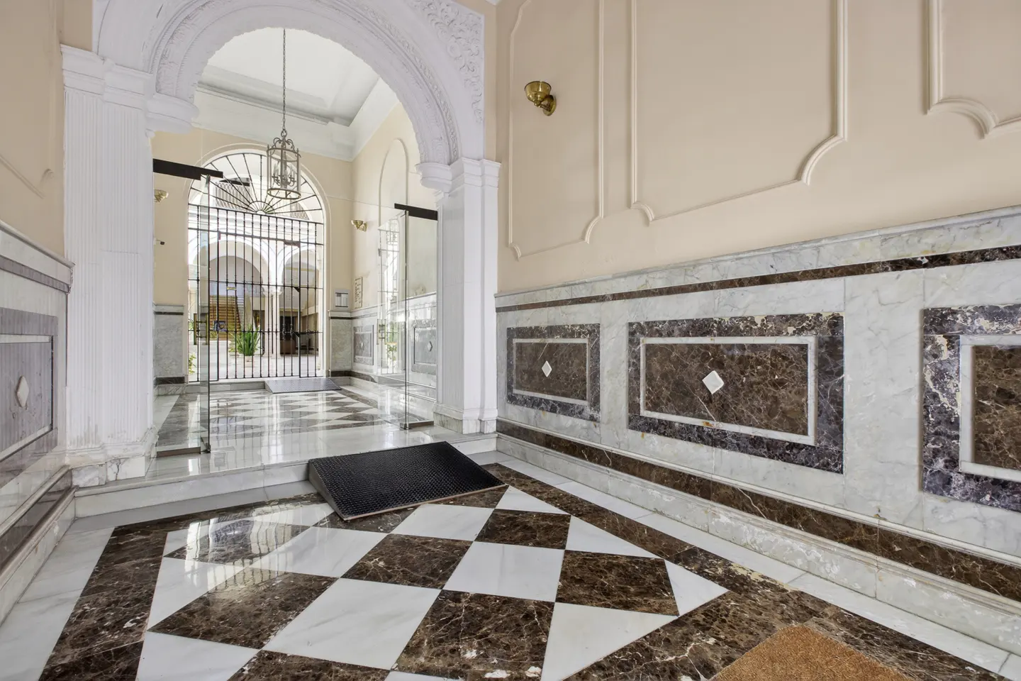Elegant building lobby with black and white checkered marble floor, arched doorway, and decorative wall paneling.