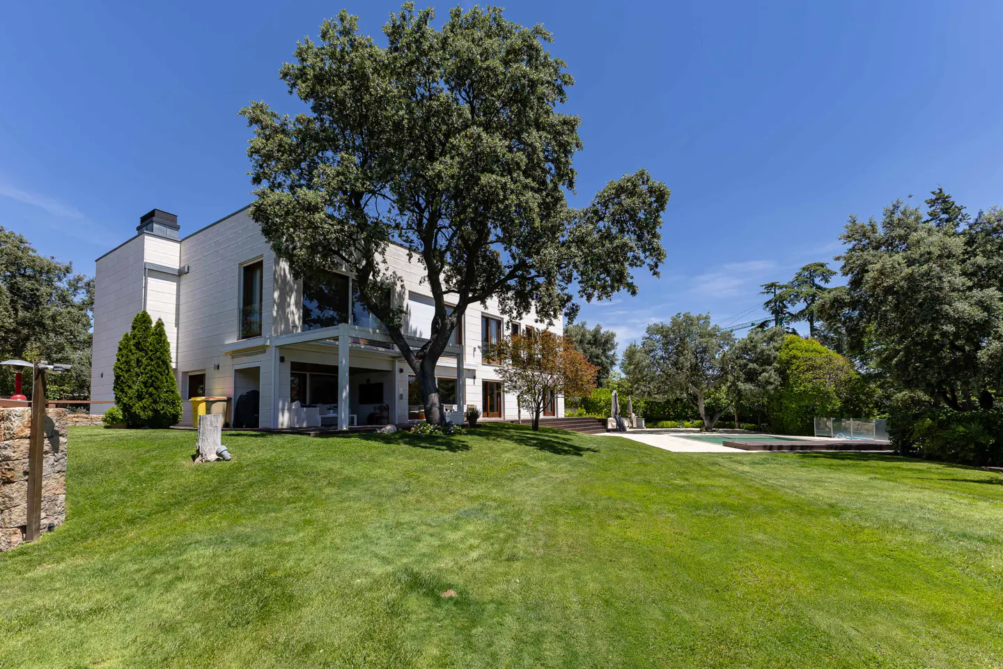 Exterior view of a modern white house with a large green lawn and mature trees under a clear blue sky.