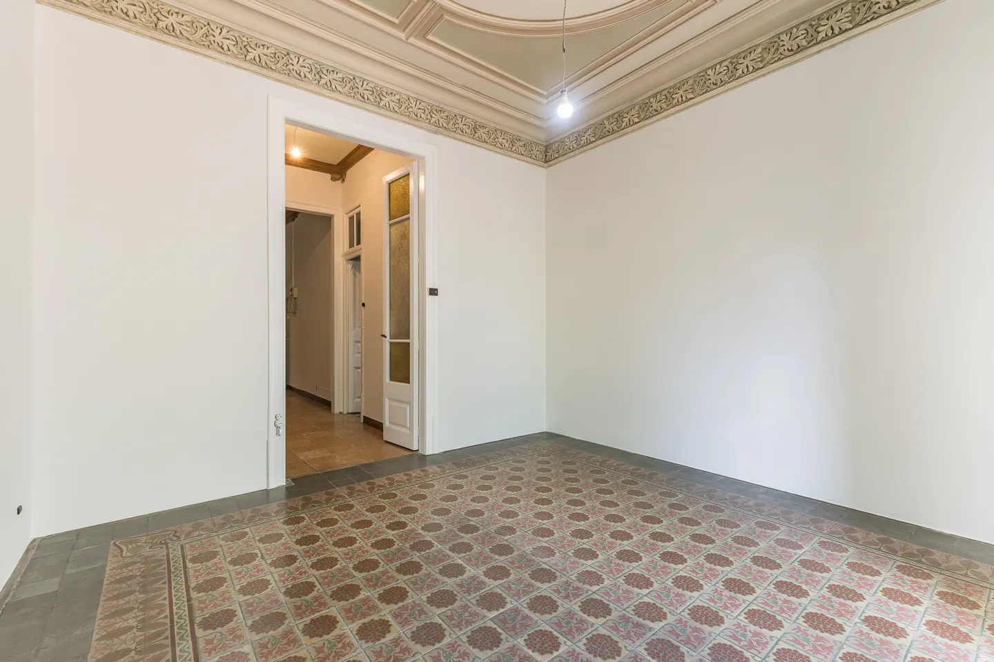 Empty room with white walls, patterned tile floor, and decorative ceiling molding. A doorway leads to a hallway.