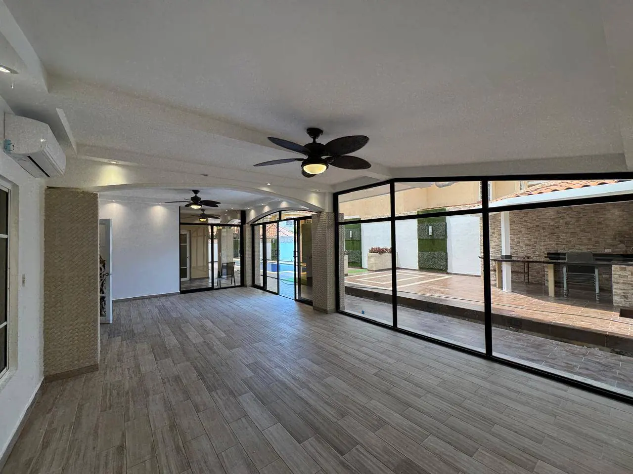 A bright sunroom with wood-look tile floors and black-framed windows overlooking a patio. Two ceiling fans are visible.