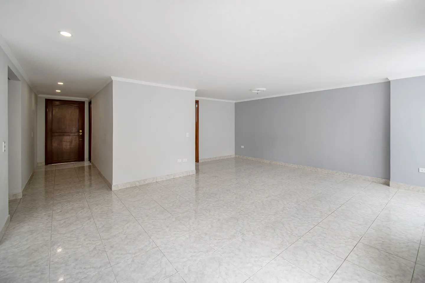 Empty room with white tile floor, light gray walls, and a dark wood door on the left.