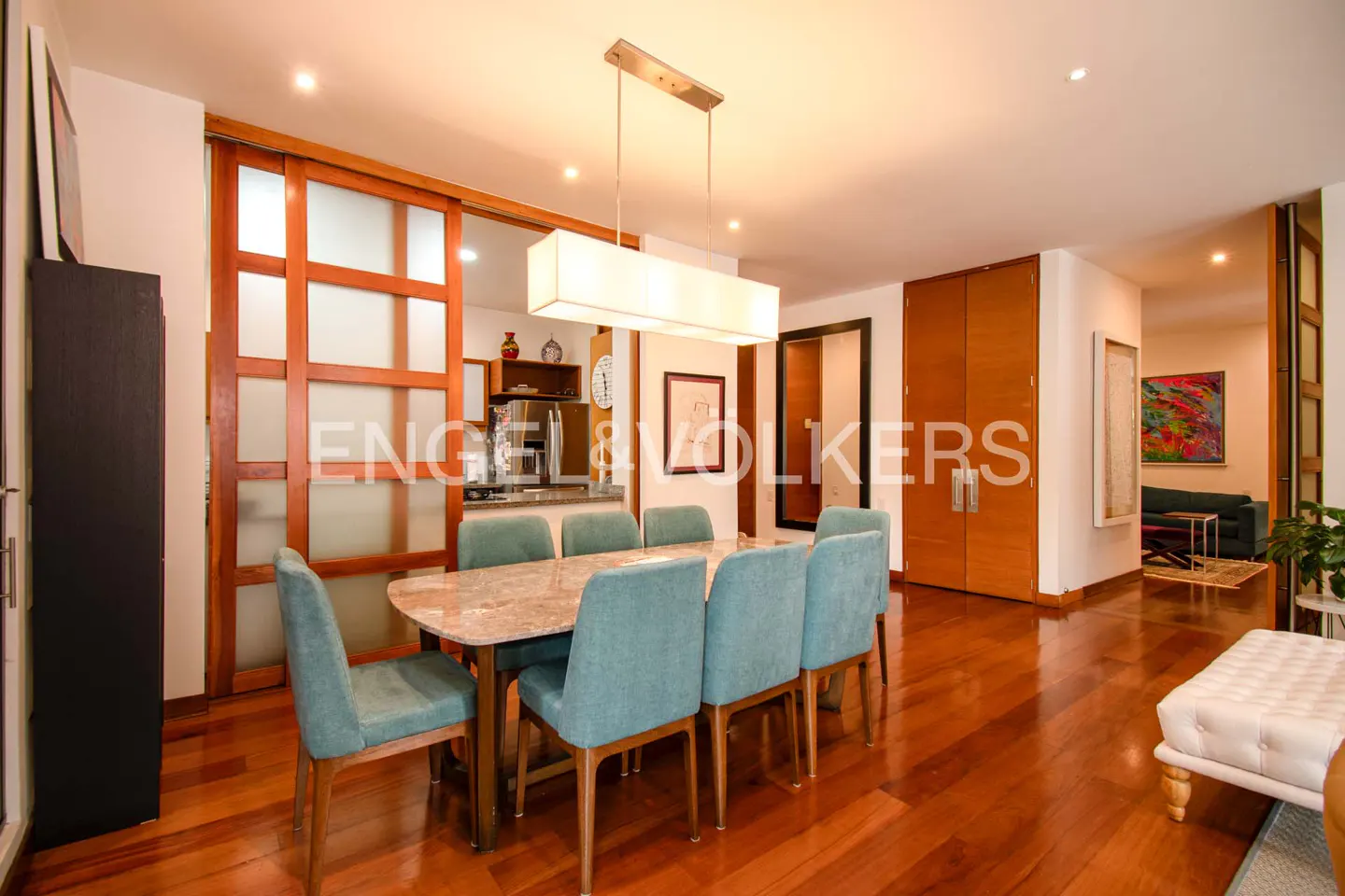 A dining room with a marble table, blue chairs, and wood floors. A modern light fixture hangs above the table.