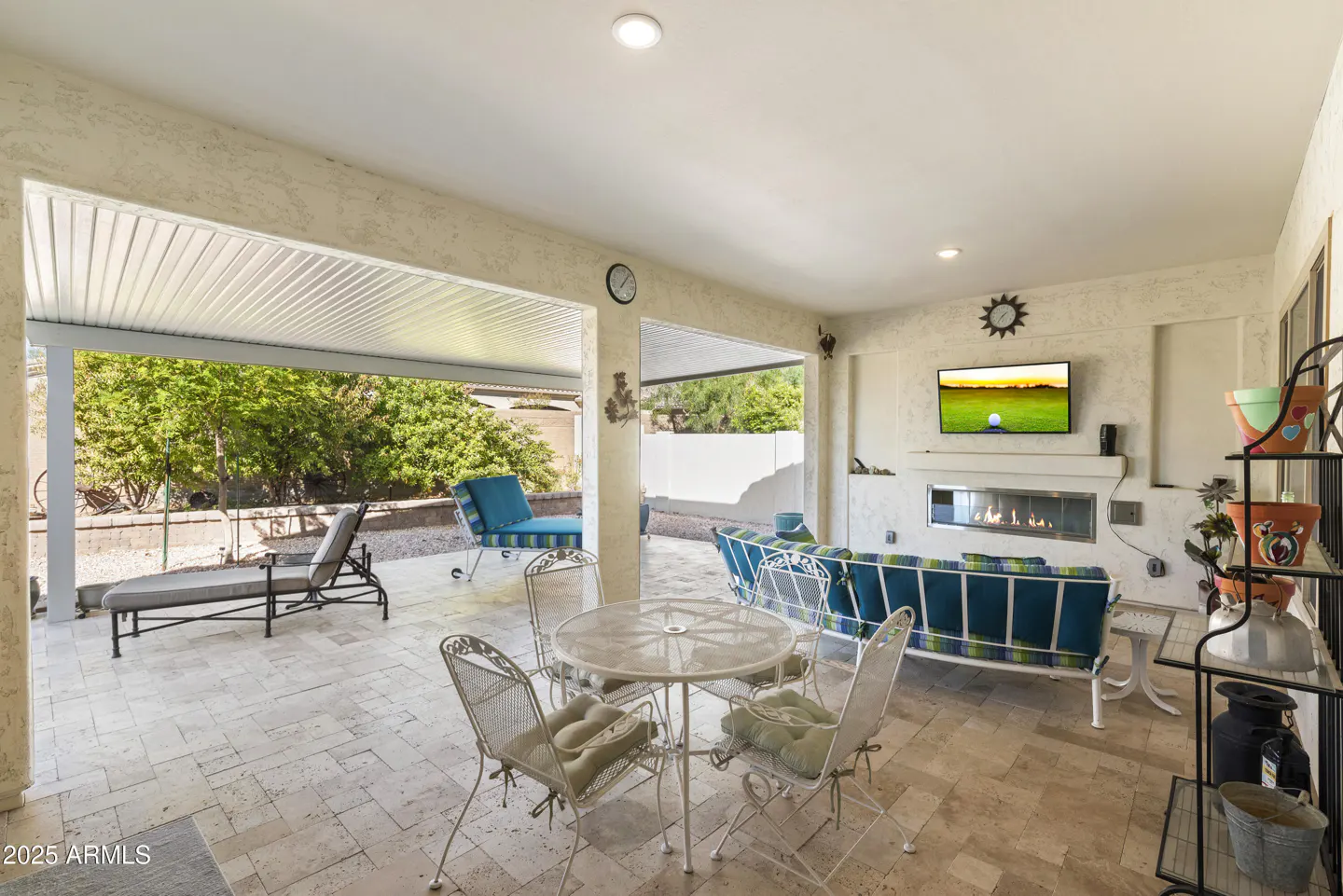 Covered patio with travertine tile, outdoor furniture, fireplace, and TV showing a golf course.