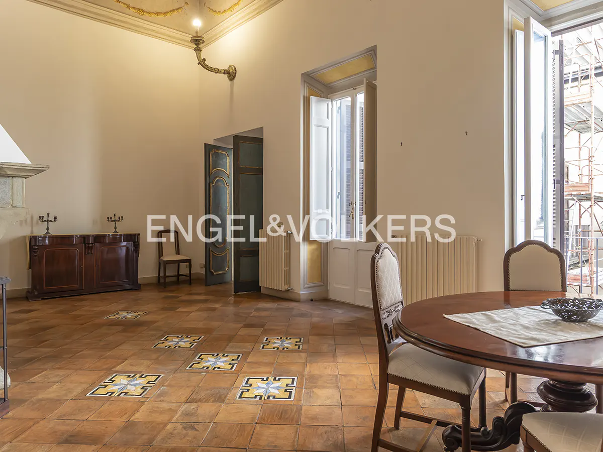 A spacious room with a round wooden table and chairs, tiled floor, and large windows.