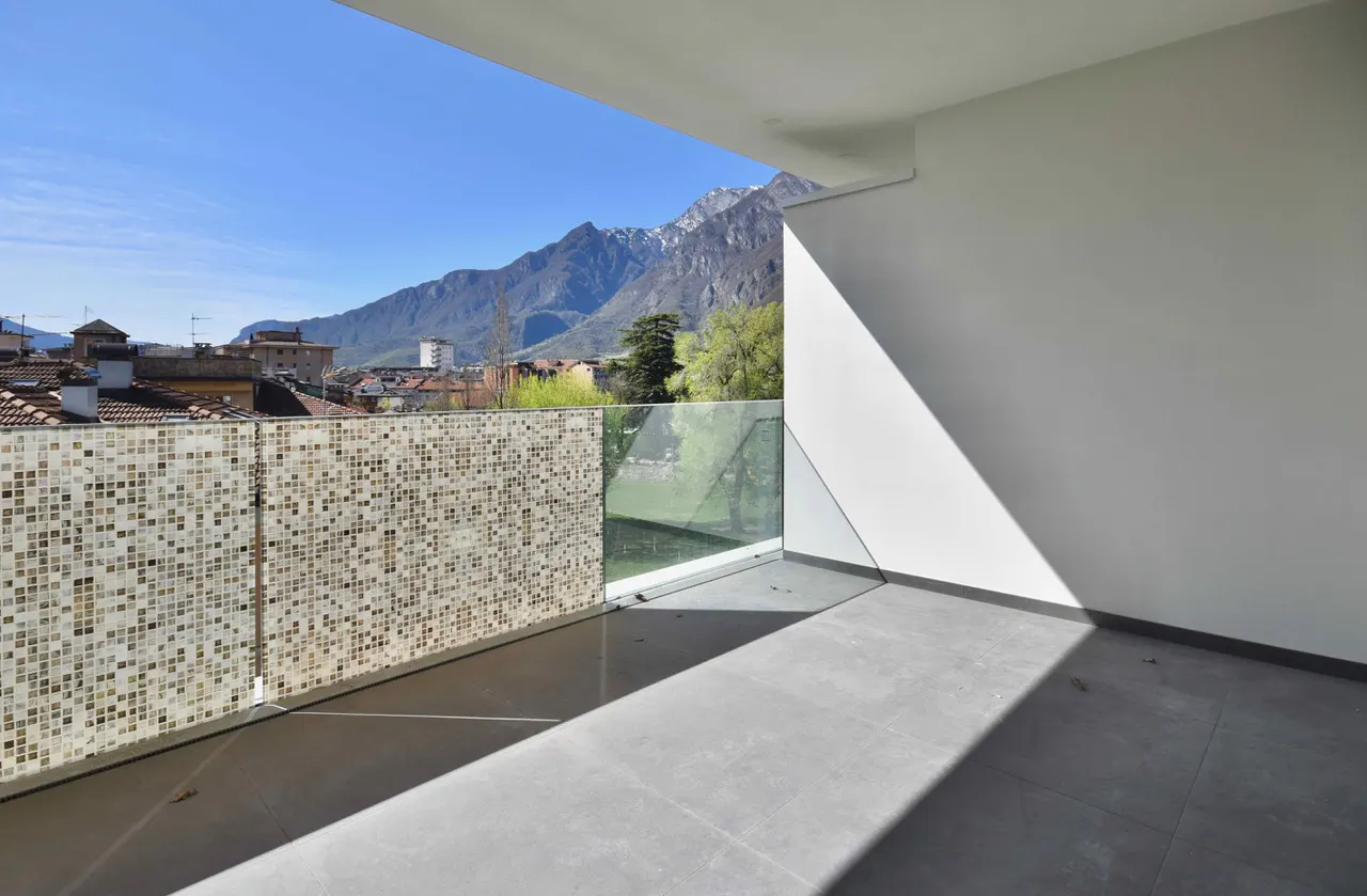 Balcony view: mosaic wall, glass railing, gray tile floor, white wall, mountain backdrop.