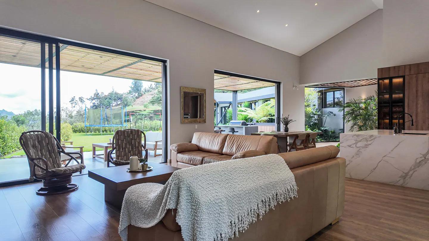 Living room with brown leather sofas, wood floors, and large sliding glass doors to a green lawn with a trampoline.