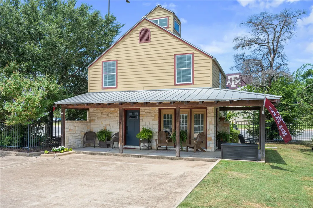 Two-story tan house with a covered porch, stone pillars, and a Texas A&M flag.