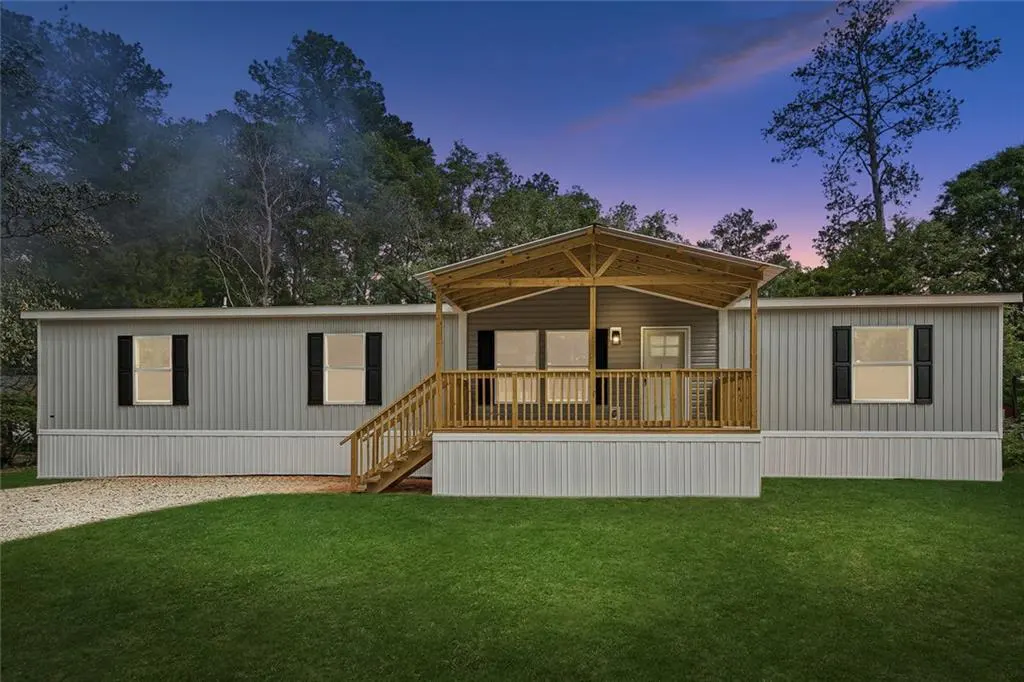 Exterior view of a gray, single-story home with a wooden porch and green lawn at dusk.