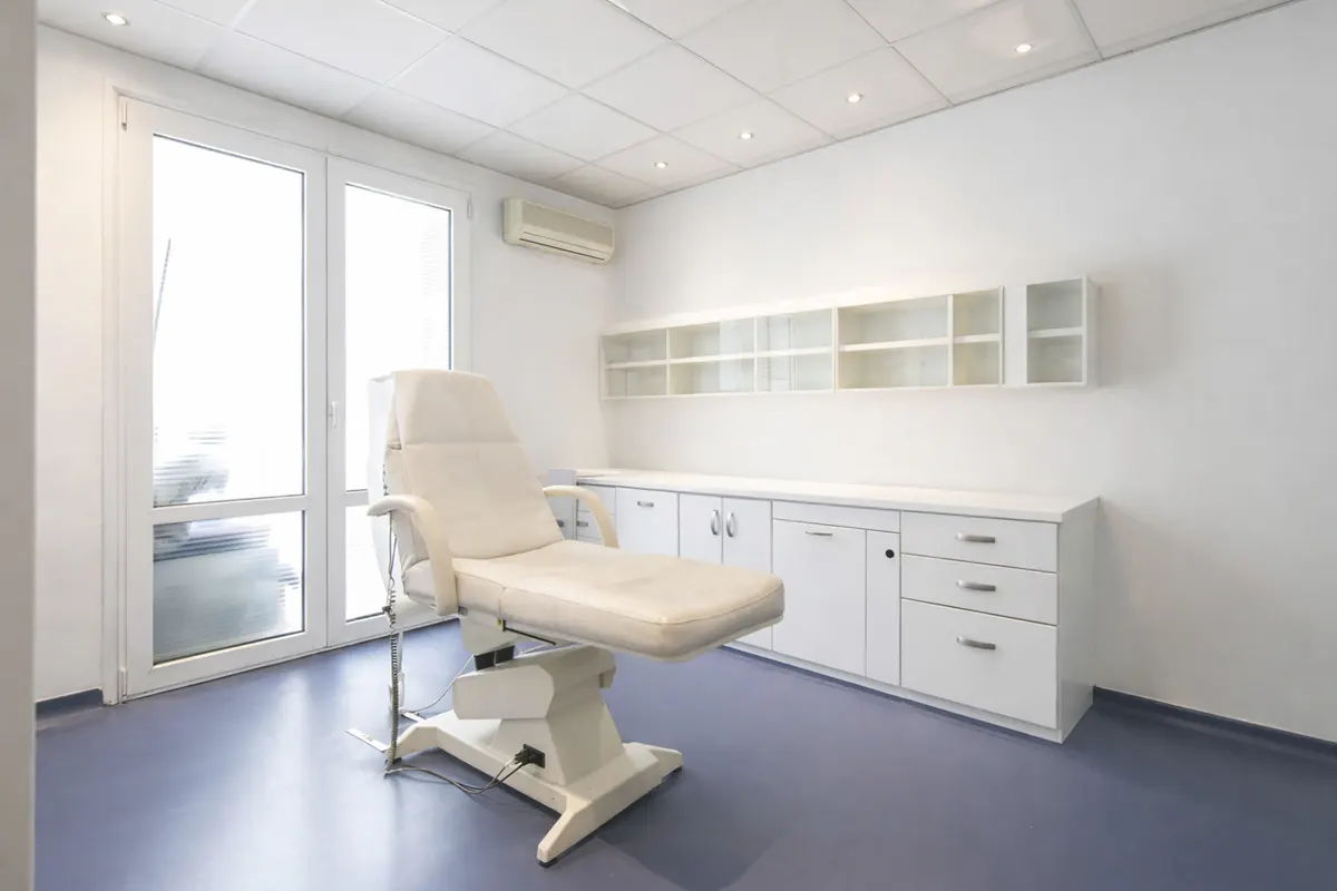 A bright, clean medical room with a white examination table, cabinets, and blue floor.