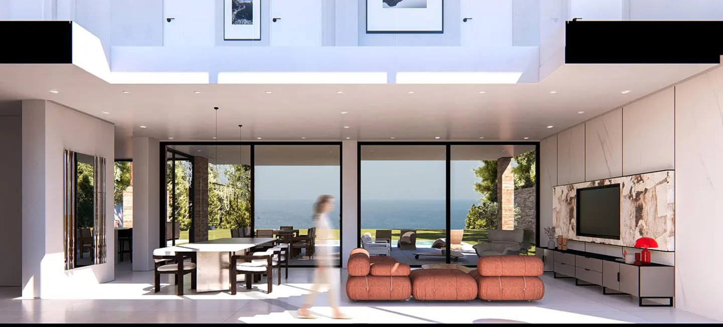 Bright, modern living space with a dining table, orange sofa, and large windows overlooking the ocean. A blurred figure walks through the room.