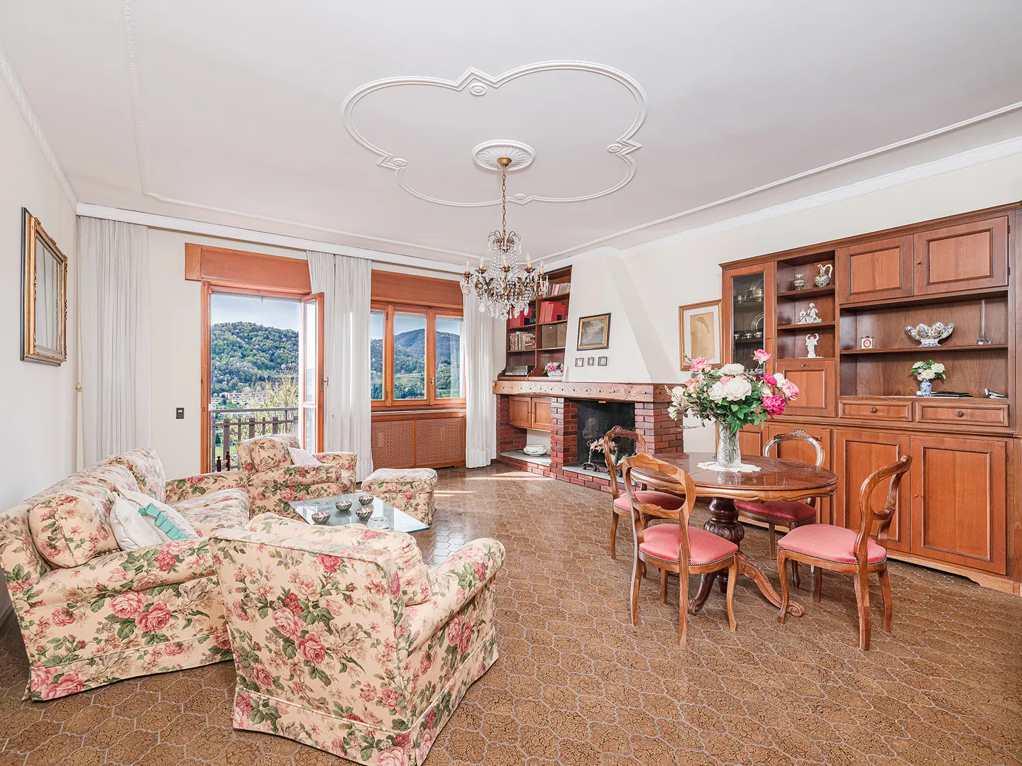 A living room with floral sofas, a fireplace, and a dining table with pink chairs.