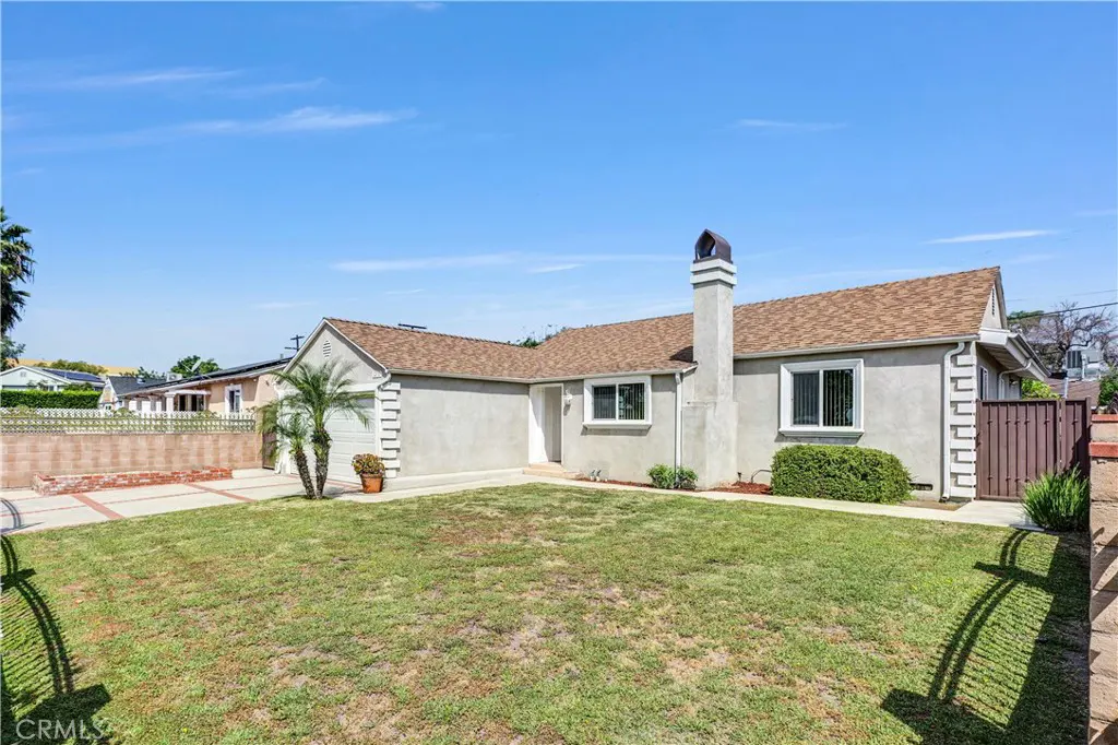 Exterior view of a single-story home with a brown roof, gray stucco, a chimney, and a green lawn under a blue sky.