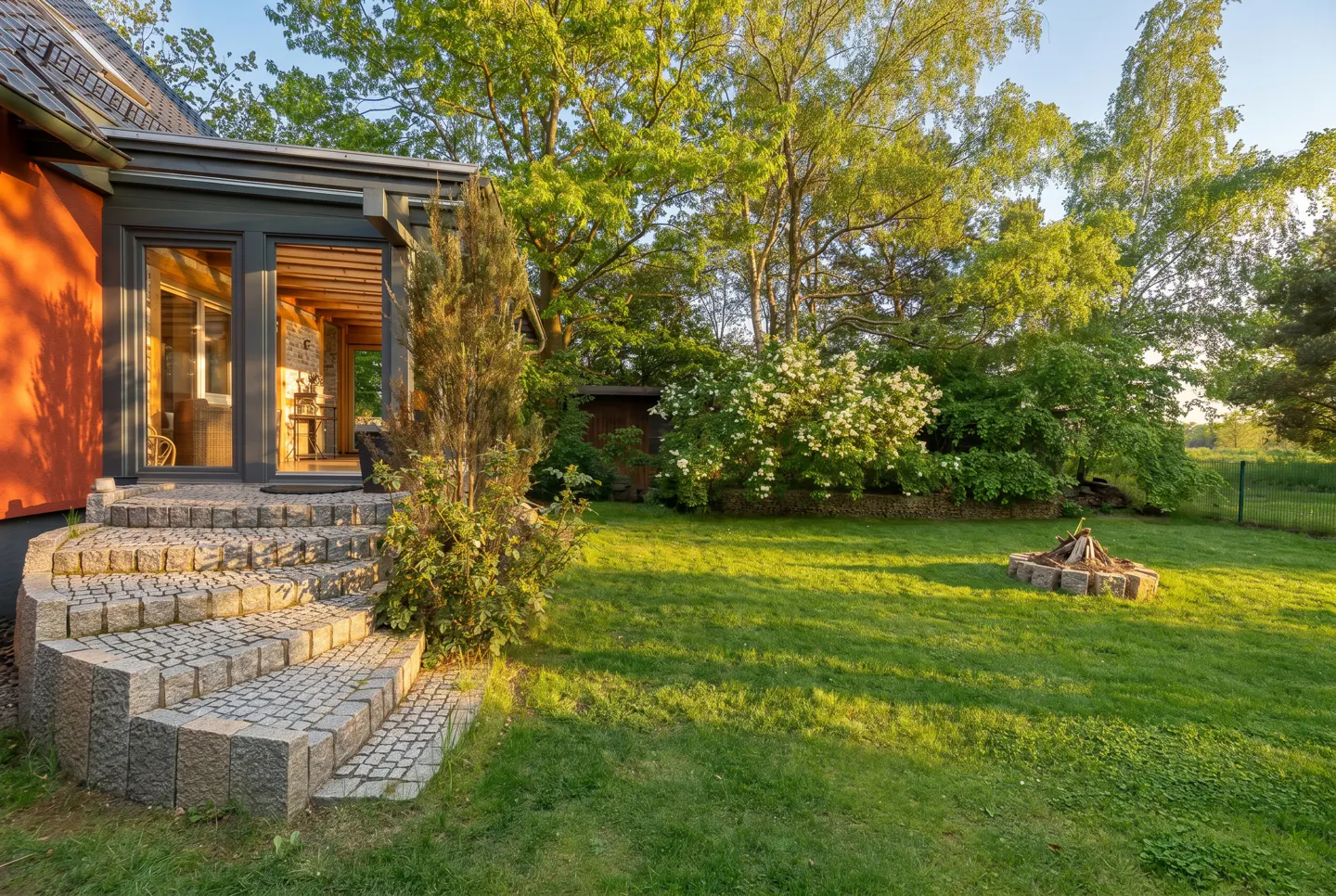 Exterior view of a house with stone steps leading to a sunroom, a green lawn, and a fire pit.
