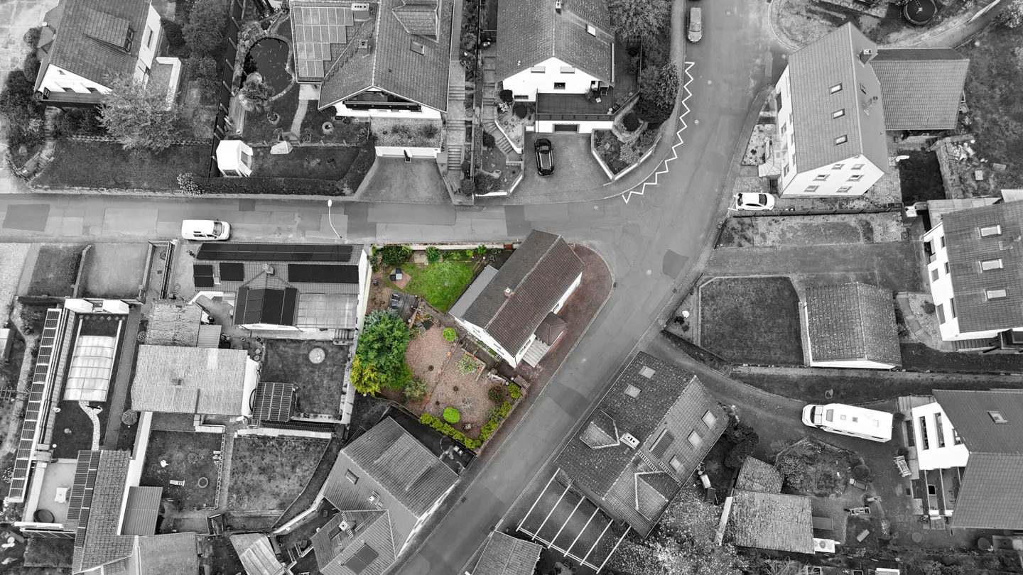 Aerial view of a house with a green lawn in a grayscale neighborhood.