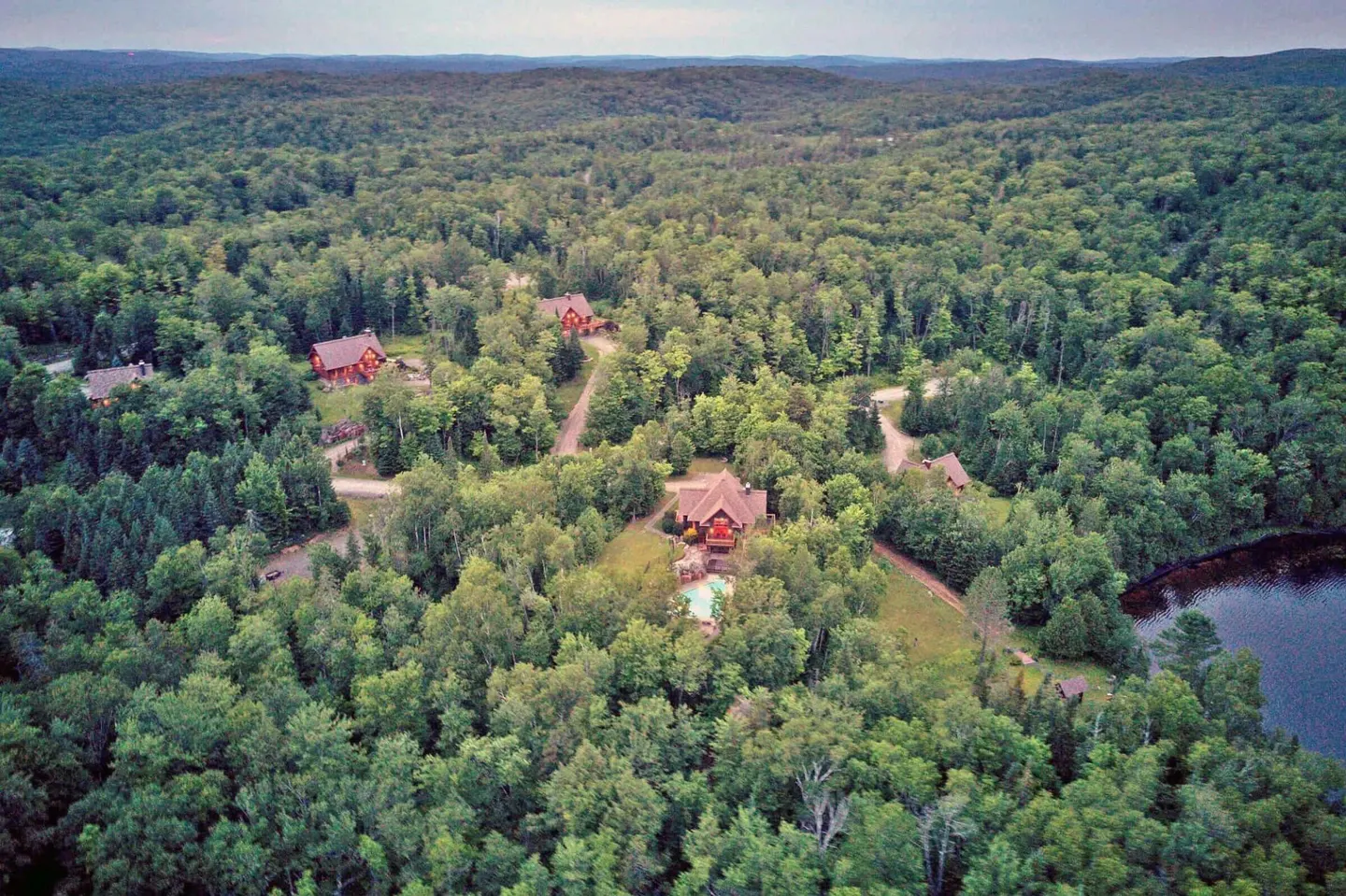 Aerial view of several red cabins nestled in a dense green forest near a lake.