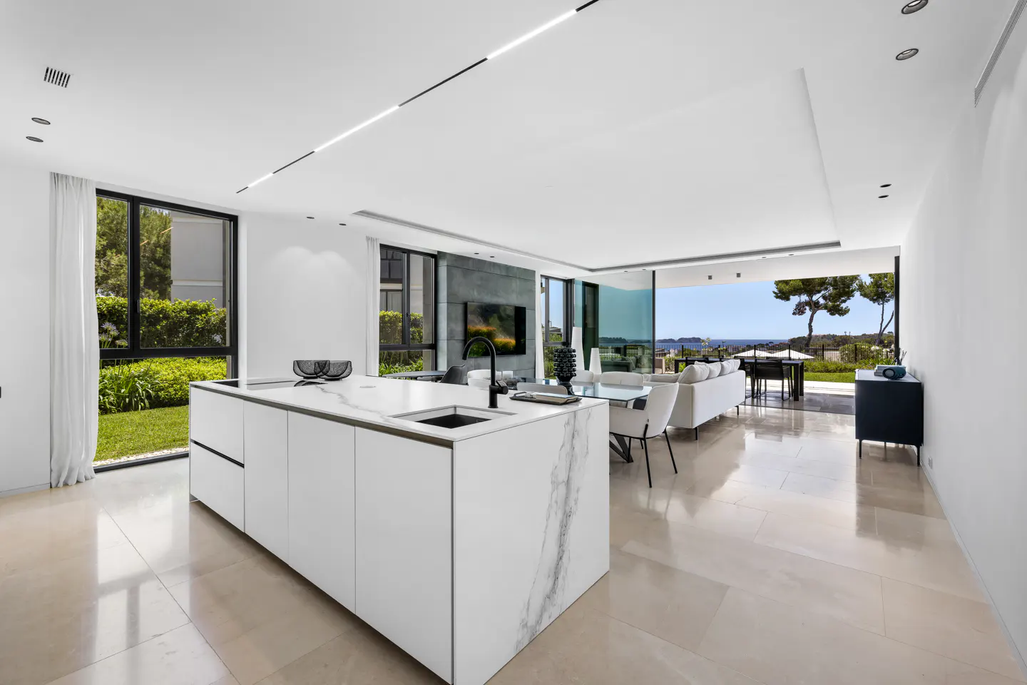 Modern open-plan kitchen with white marble island, sleek living area, and floor-to-ceiling windows overlooking the ocean.