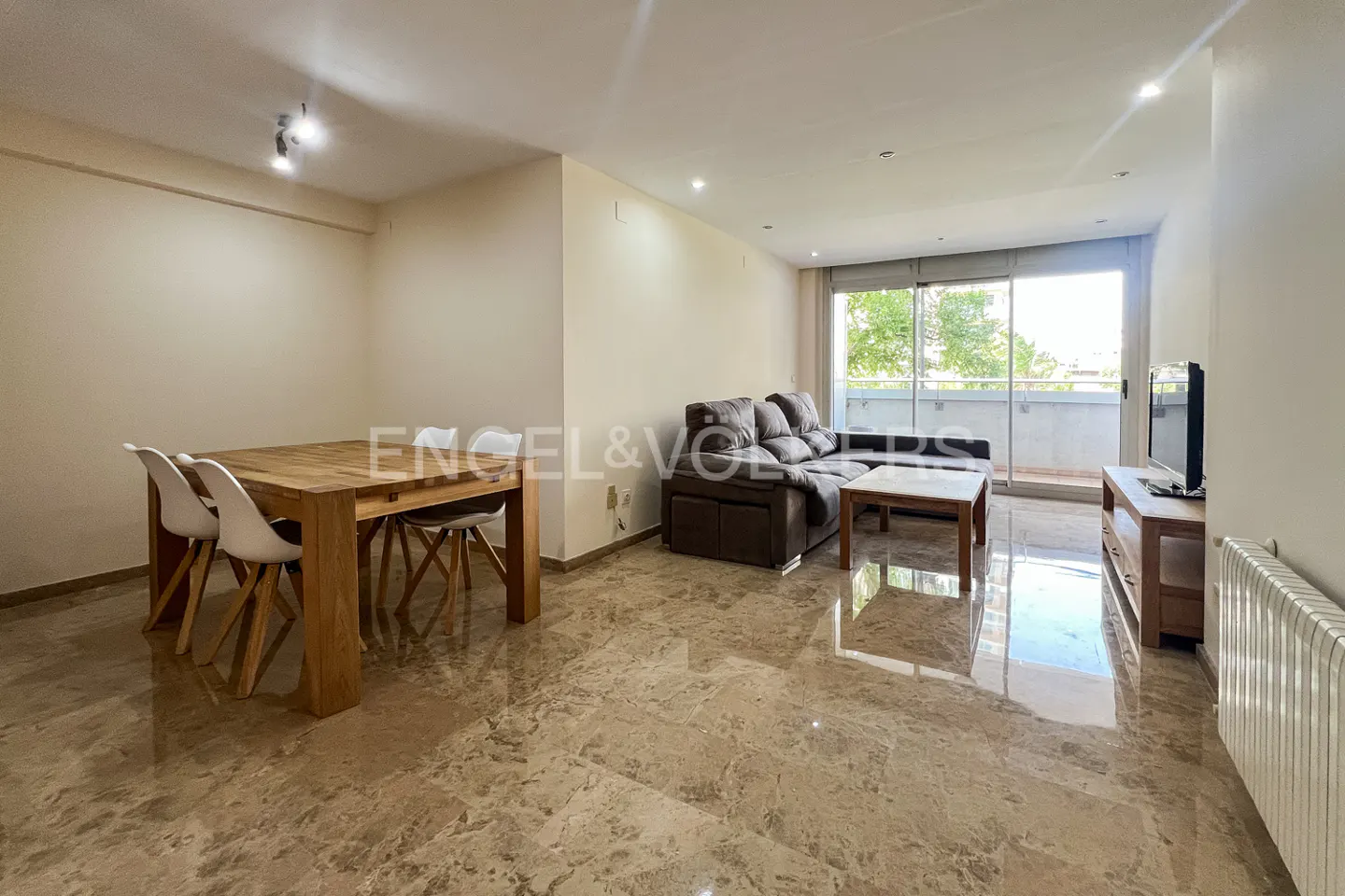 Open-concept living space with a wood dining table, brown sofa, and balcony access. Marble floors reflect light.