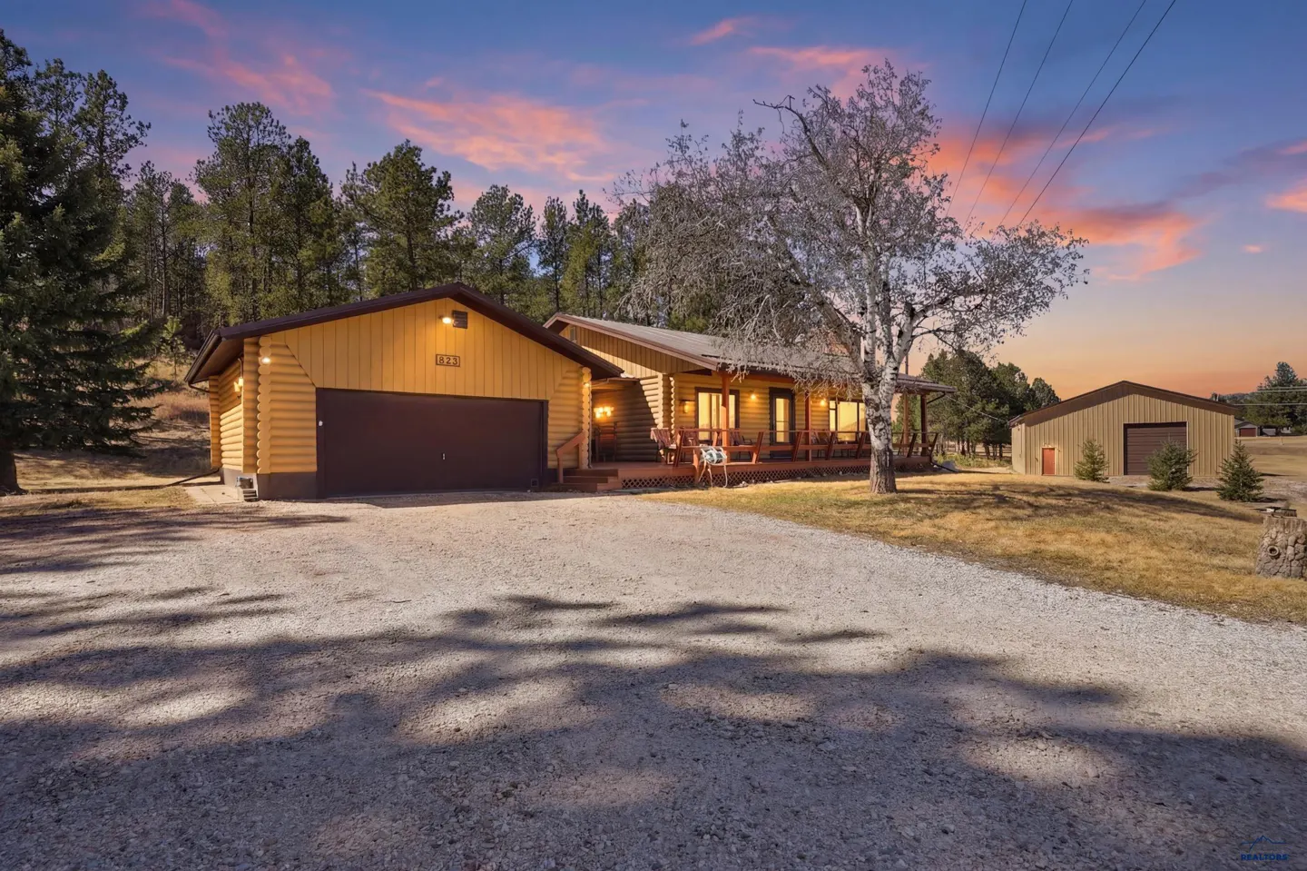 Exterior of a log cabin home with a garage and a gravel driveway at sunset.