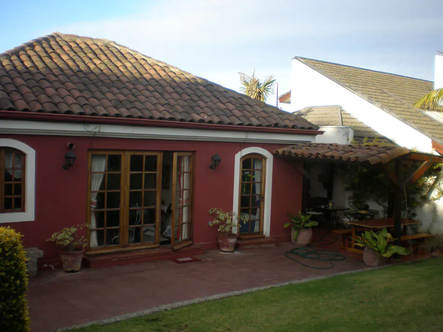 Exterior of a red house with a terracotta tile roof, patio, and green lawn. Wooden doors and windows add warmth.