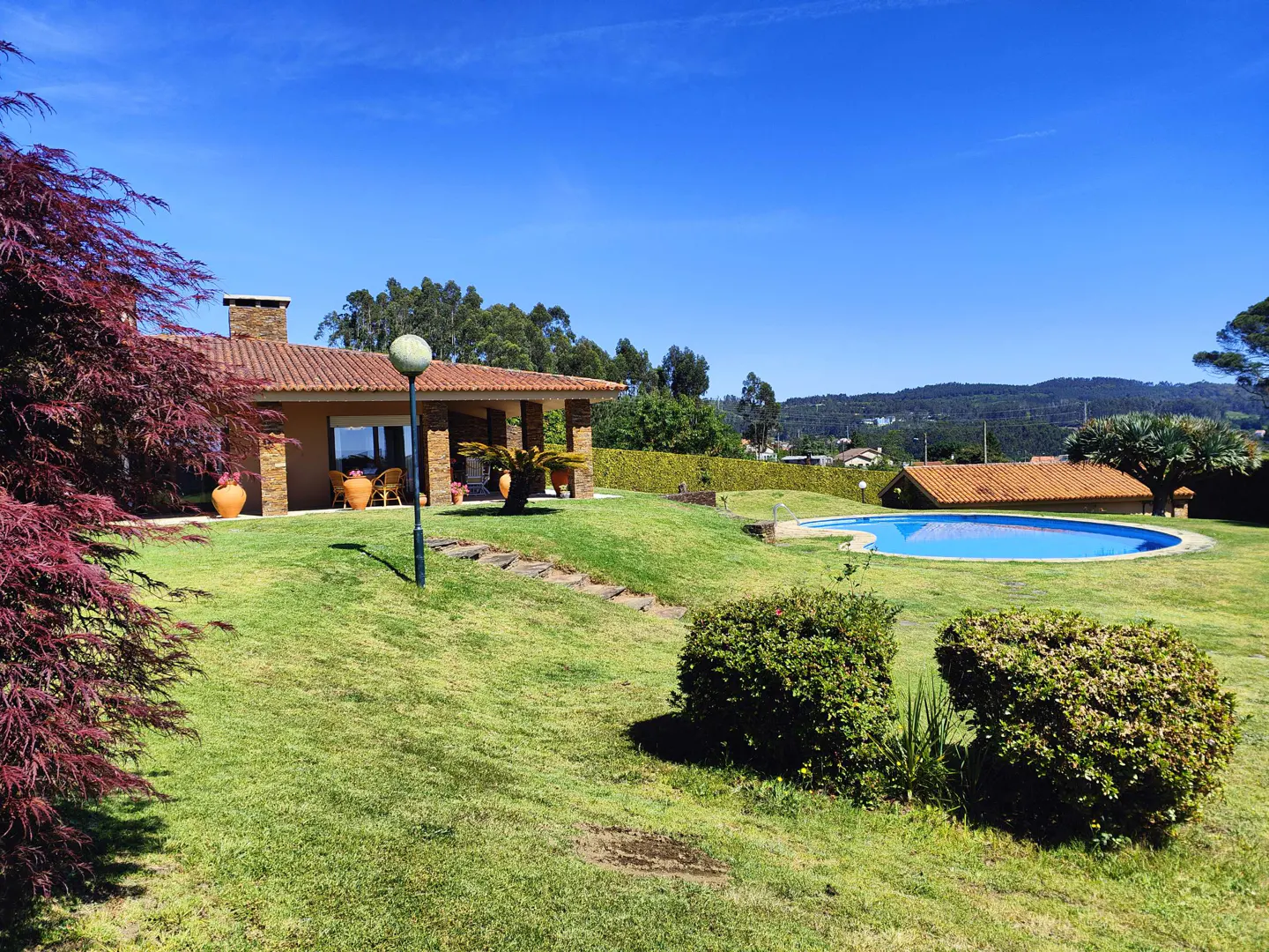 Exterior of a tan house with a red tile roof, a pool, and a green lawn under a blue sky.