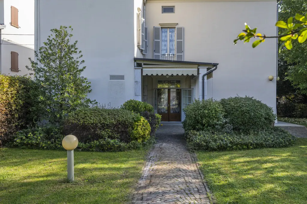 Exterior view of a white house with a brick path leading to the front door, surrounded by green bushes and grass.