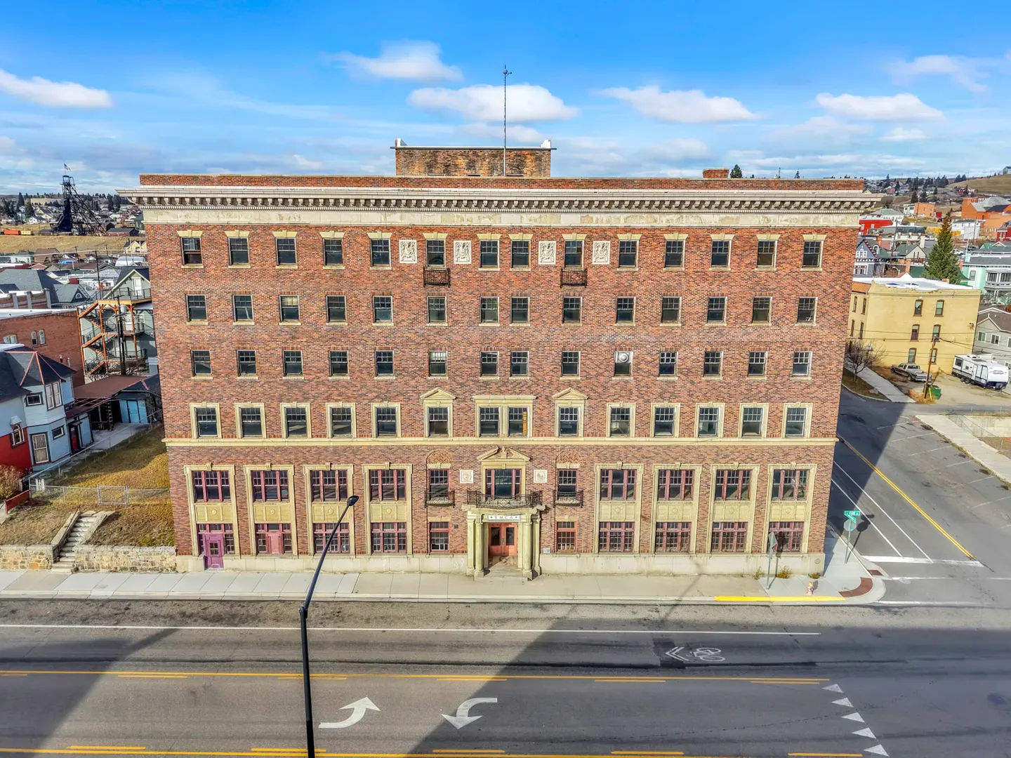 A five-story brick building with many windows, a street in front, and a blue sky above.