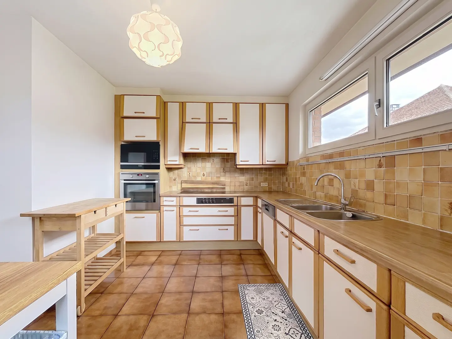 Bright kitchen with white and wood cabinets, brown tile floor, and a wooden island. A window lets in natural light.