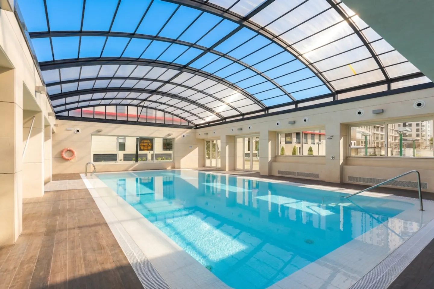Indoor pool with a clear domed roof, light blue water, and beige walls. A life preserver hangs on the wall.