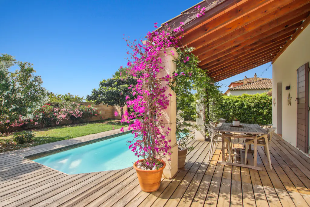 Wooden deck with a dining table, a swimming pool, and a stone pillar covered in vibrant pink bougainvillea flowers.