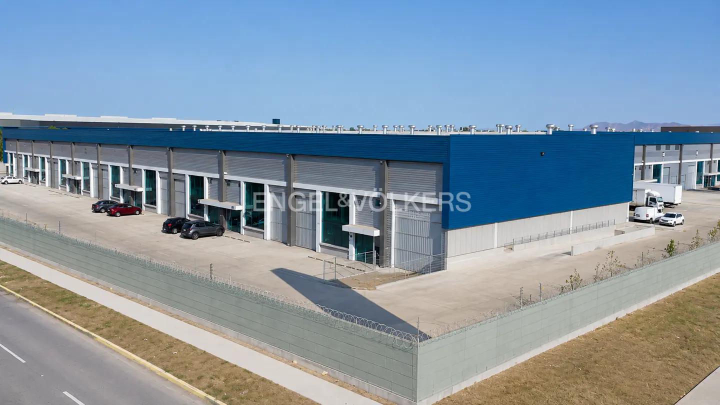 Aerial view of a blue and gray Engel & Völkers industrial building with parking, a fence, and a road.