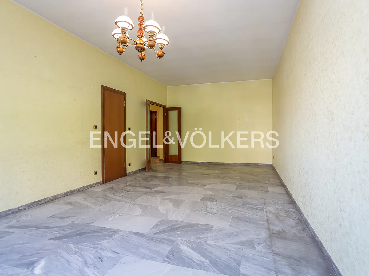 Empty room with yellow walls, marble floor, and a chandelier. Two wooden doors are visible. Engel & Völkers logo is in the center.