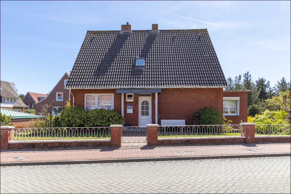 A red brick house with a dark gray tiled roof, white door, and a white metal fence.