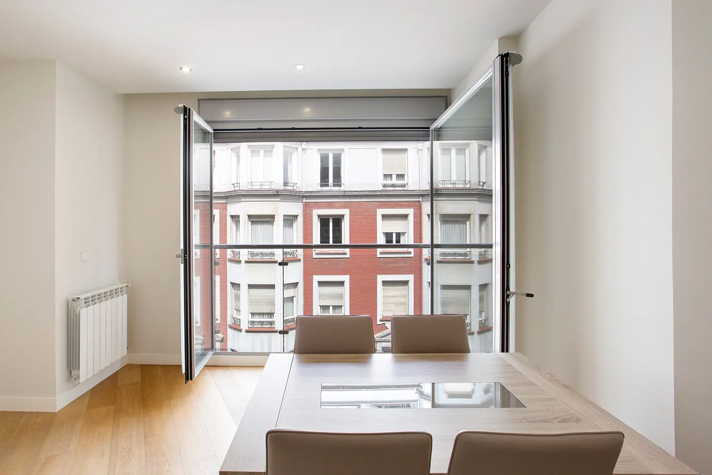 Bright room with a wooden table and chairs facing open glass doors with a view of a red and white building.
