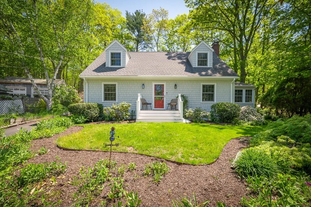 Exterior of a light gray house with a red door, white trim, and green lawn surrounded by trees.
