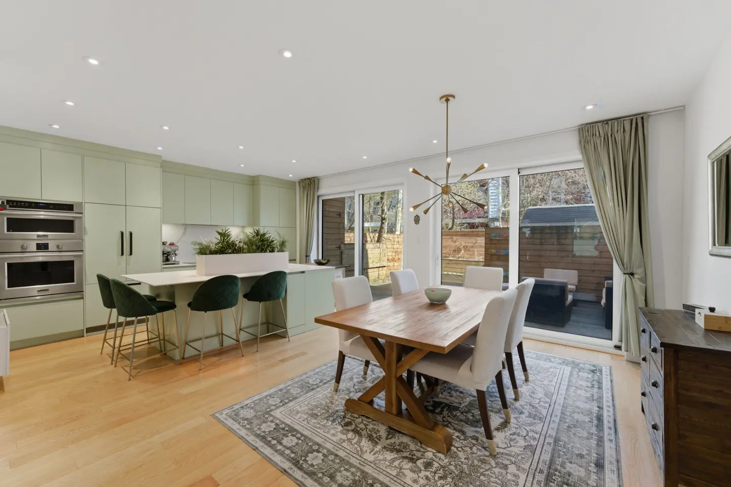 Bright, modern kitchen and dining area with light green cabinets, wood table, and sliding glass doors to a patio.