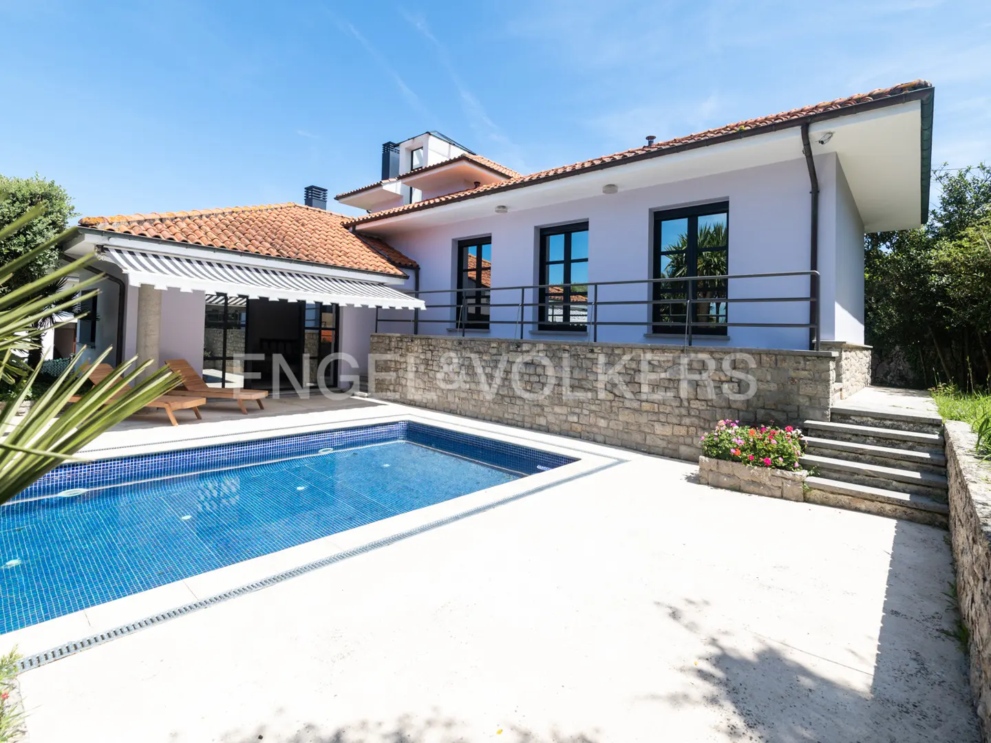 Exterior view of a light purple house with a blue tiled pool, stone wall, and orange tiled roof on a sunny day.