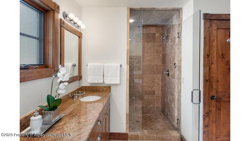 Bathroom with granite countertop, white sink, wood cabinets, and a glass-enclosed shower with brown tiles. A white orchid sits on the counter. [AI-generated text]