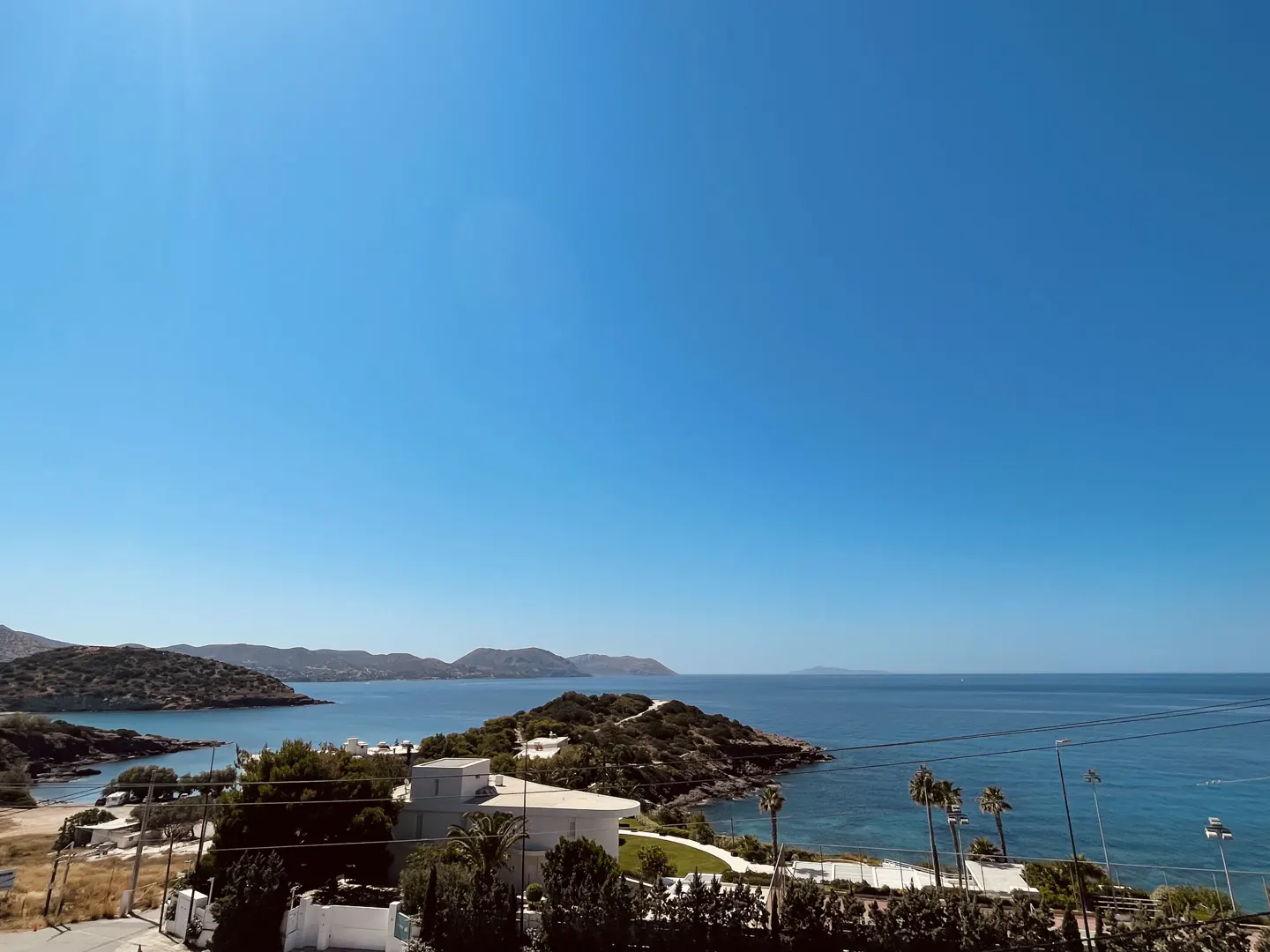Ocean view with islands, white buildings, and palm trees under a clear blue sky.