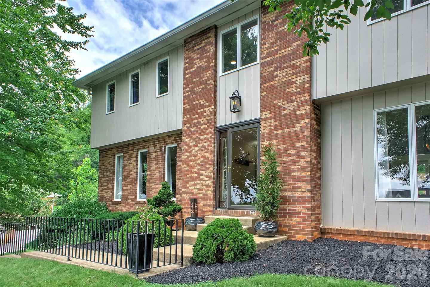 Two-story home exterior with red brick and light gray vertical siding, a glass front door, and landscaped front yard.
