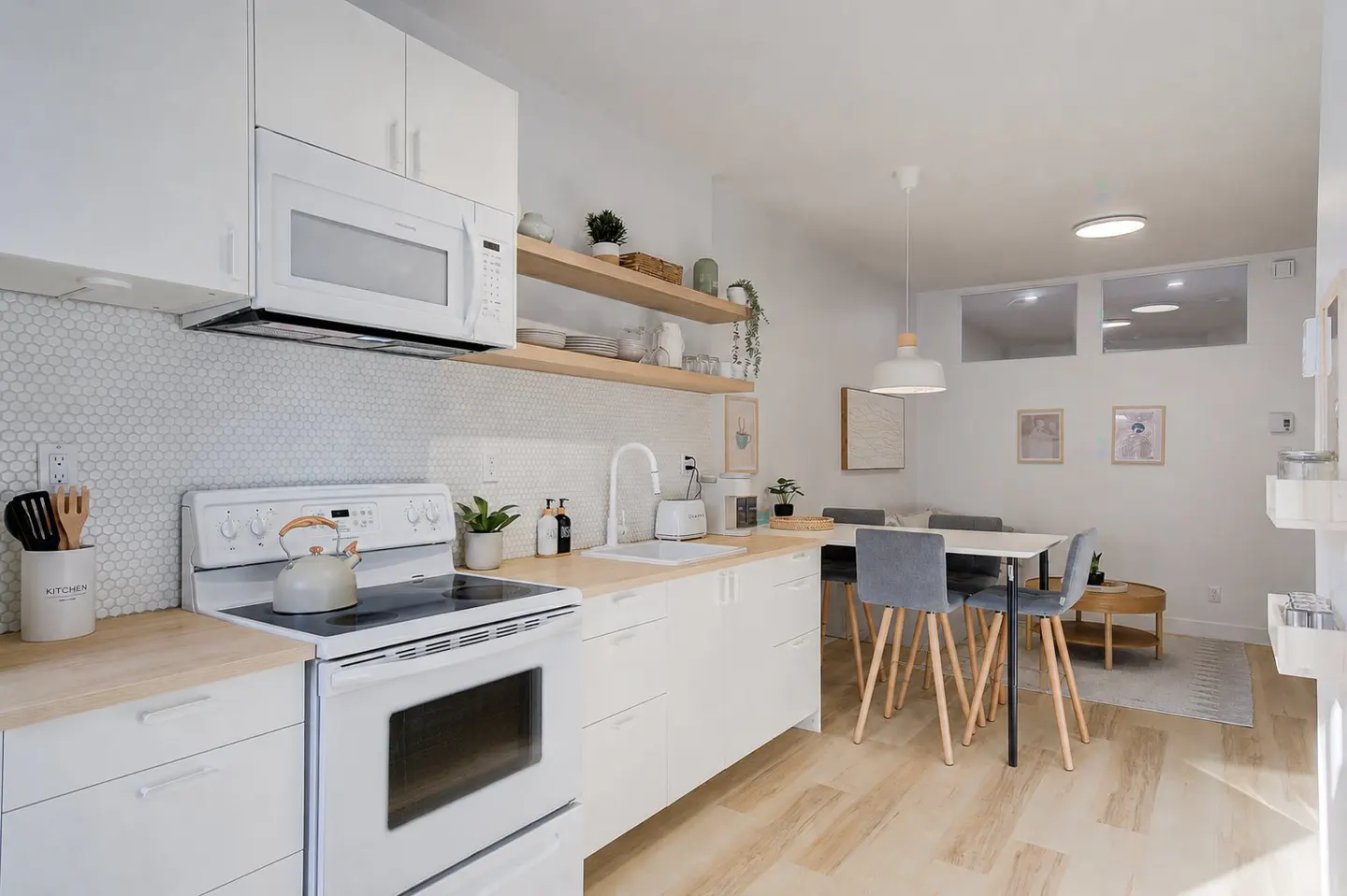 Bright, modern kitchen with white cabinets, wood countertops, and a dining area with gray chairs.