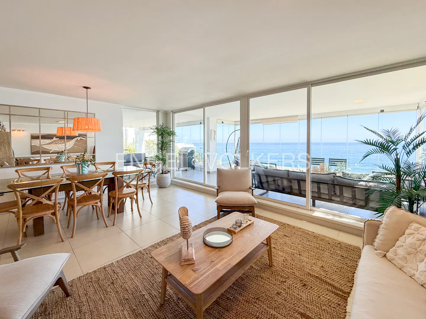 Bright living room with dining area, beige sofa, jute rug, and ocean view through large windows.